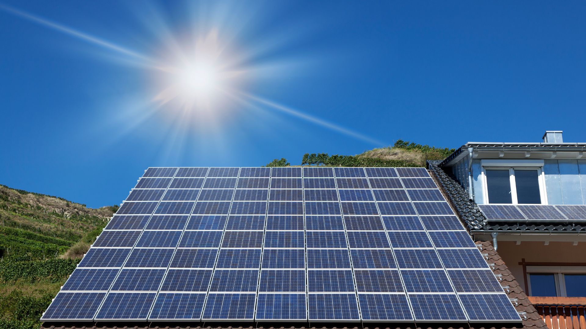 Large solar panel array on roof with bright sun and blue sky