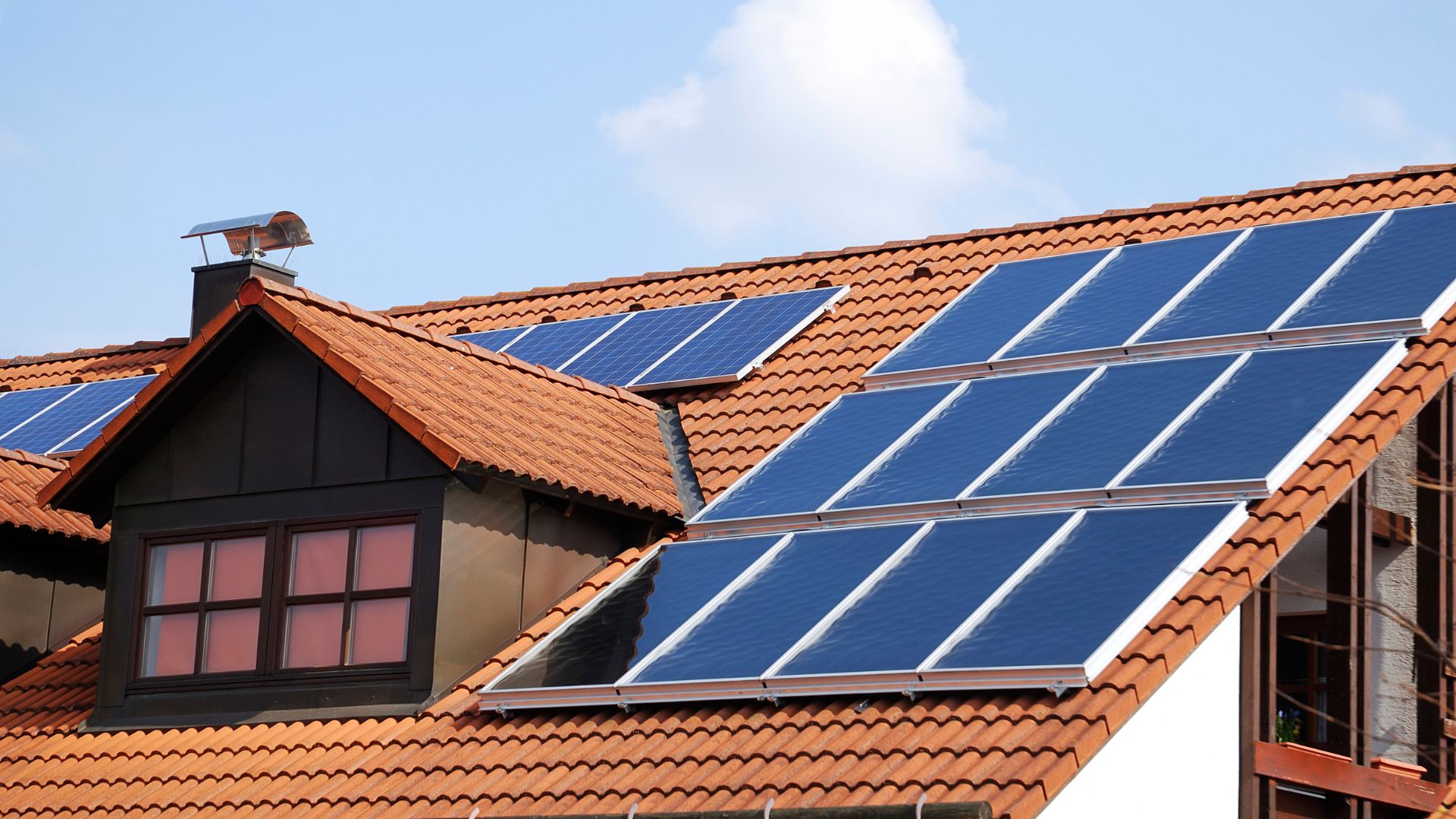 Residential roof with multiple blue solar panels on terracotta tile surface