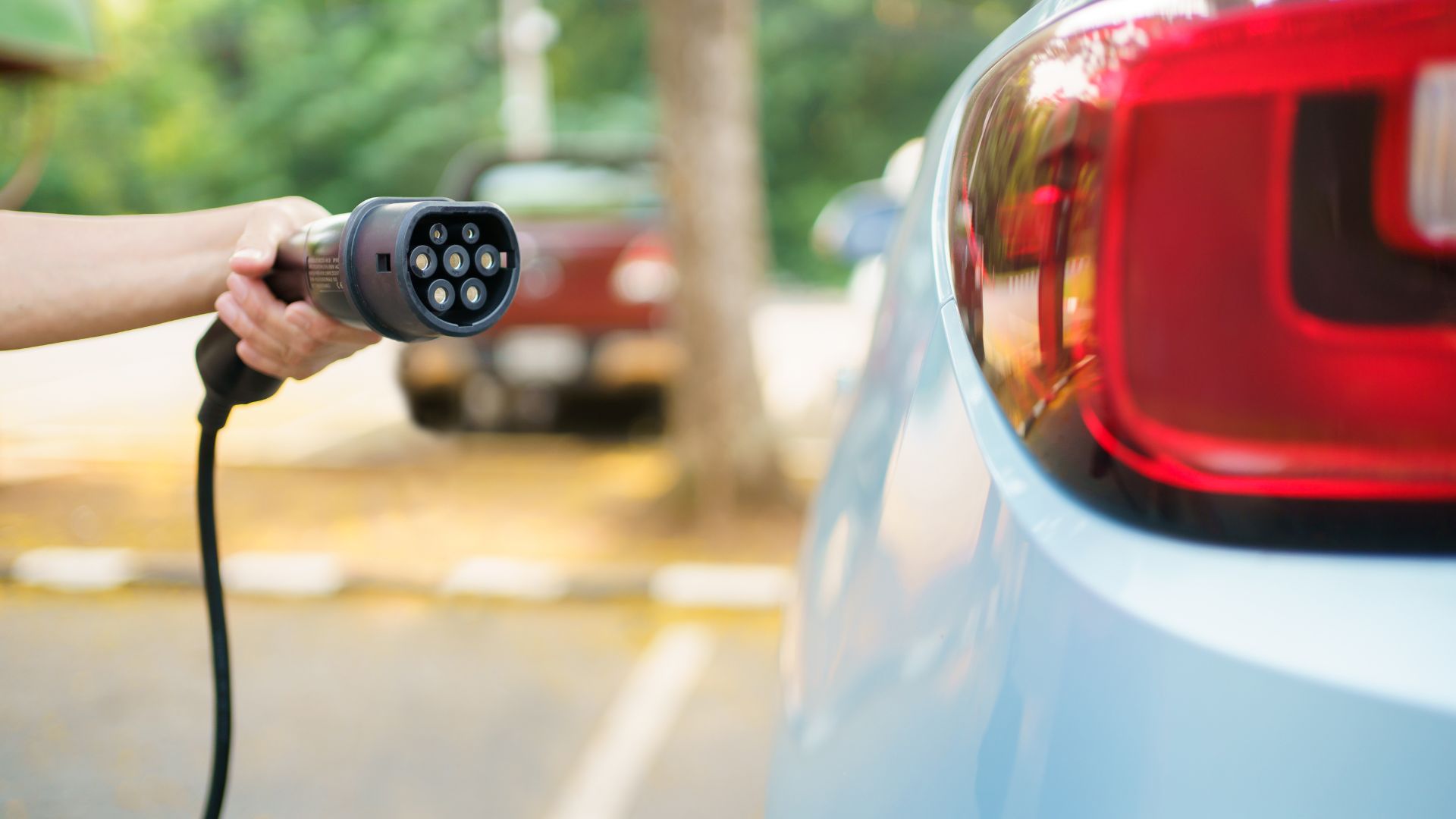 Electric vehicle charging plug connected to a light blue car