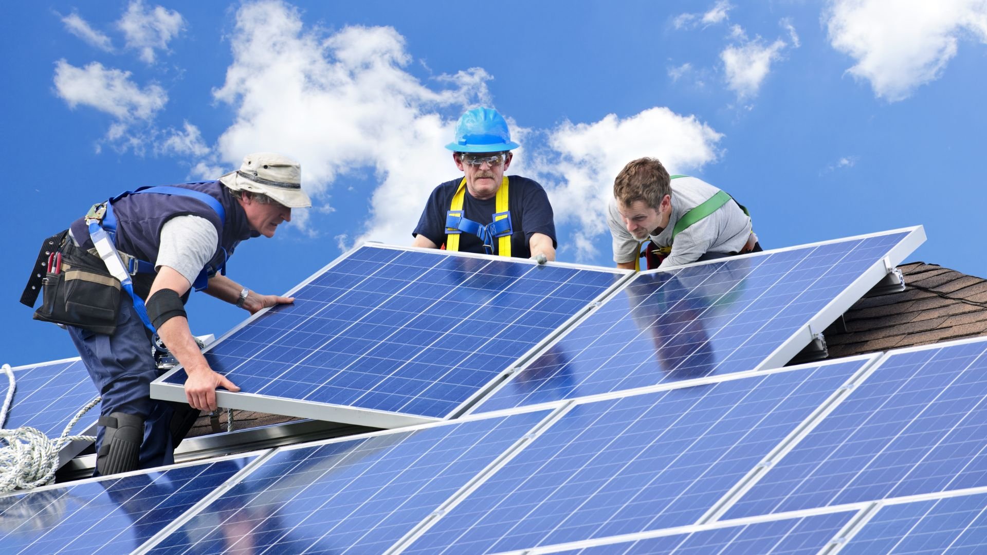 Workers installing blue solar panels on a residential rooftop under sunny sky