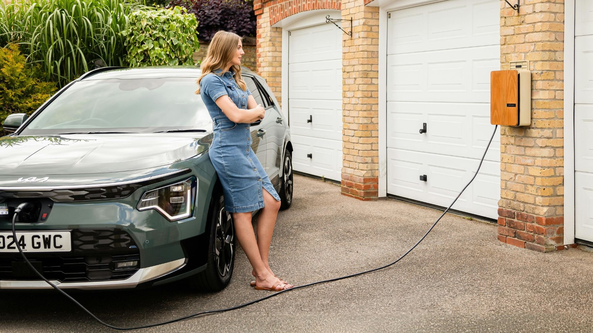Woman charging electric car at home next to white garage doors