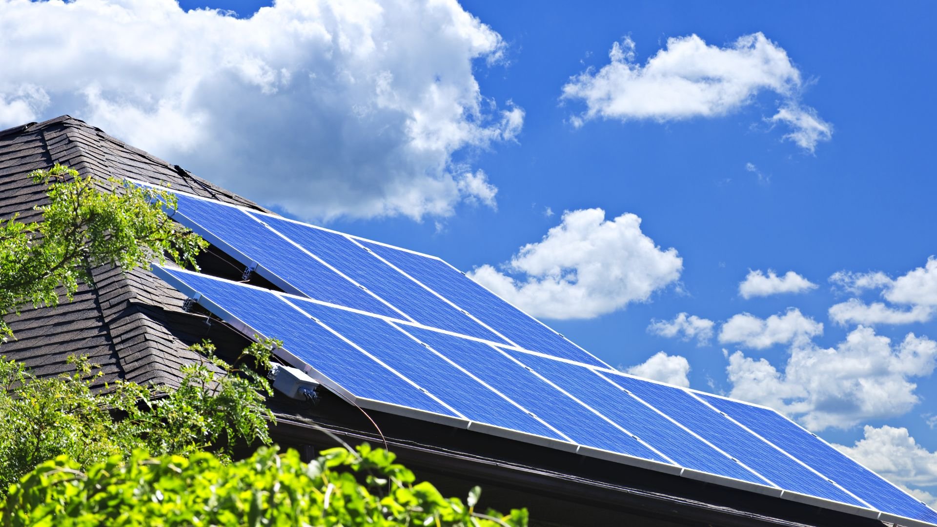 Blue solar panels installed on a house roof with fluffy clouds